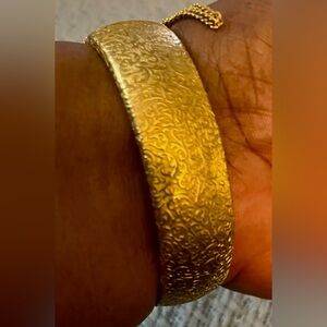 Unmarked, frosted gold tone thick bangle bracelet with security chain